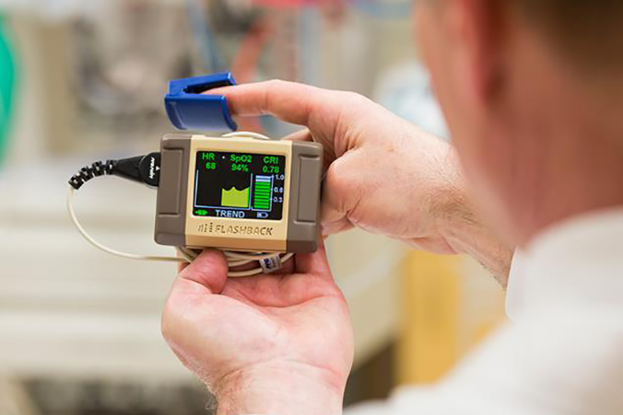 Hand-held blood loss monitor with a small cord and a clip attached to a person’s finger.