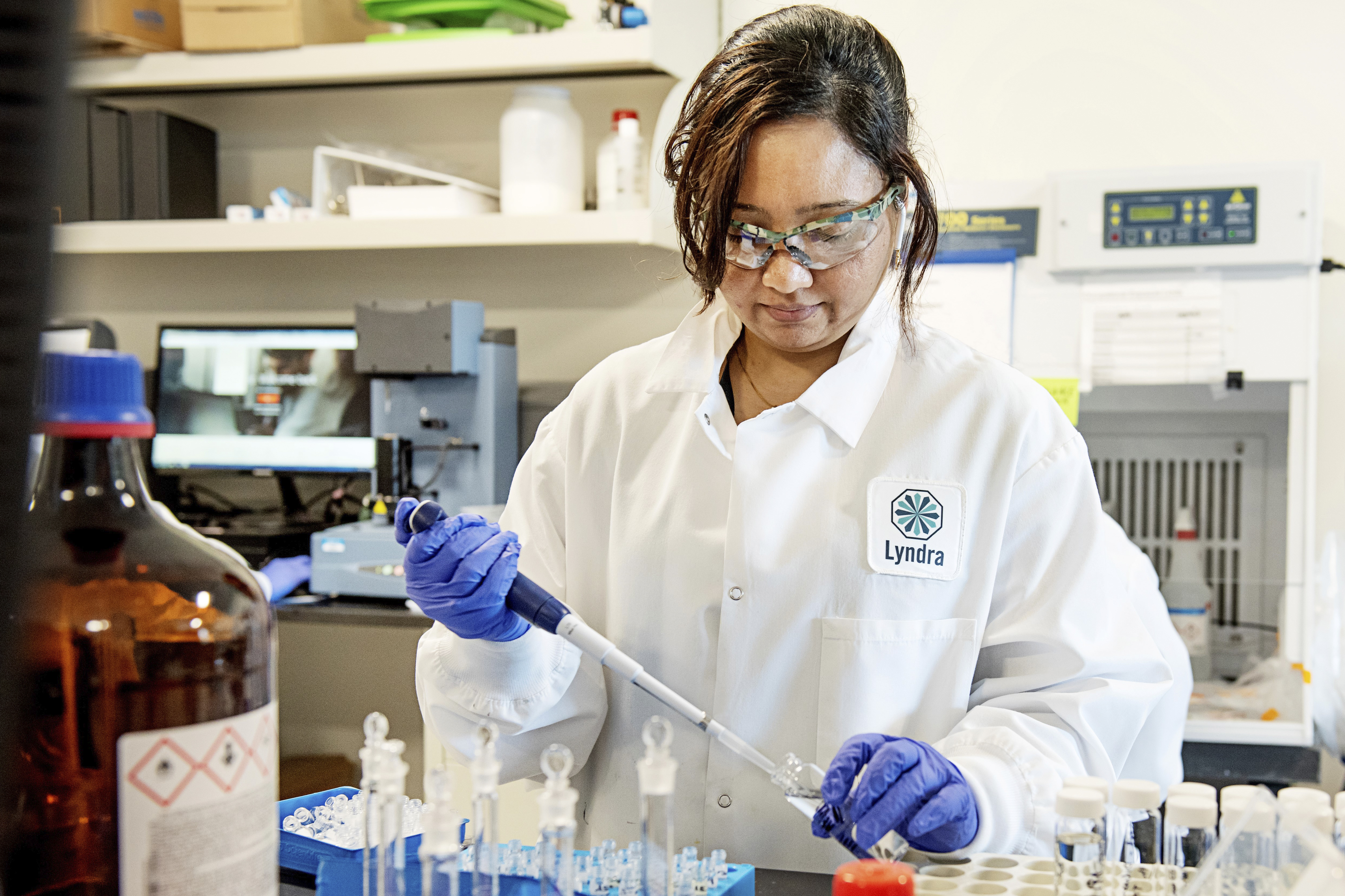 Photo of a laboratory technician using a pipette to extract liquid from a small glass bottle