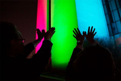 P.J. Brooks, Ph.D., and Joni L. Rutter, Ph.D., raising their hands in front of the lit-up Building 38A on the NIH main campus.